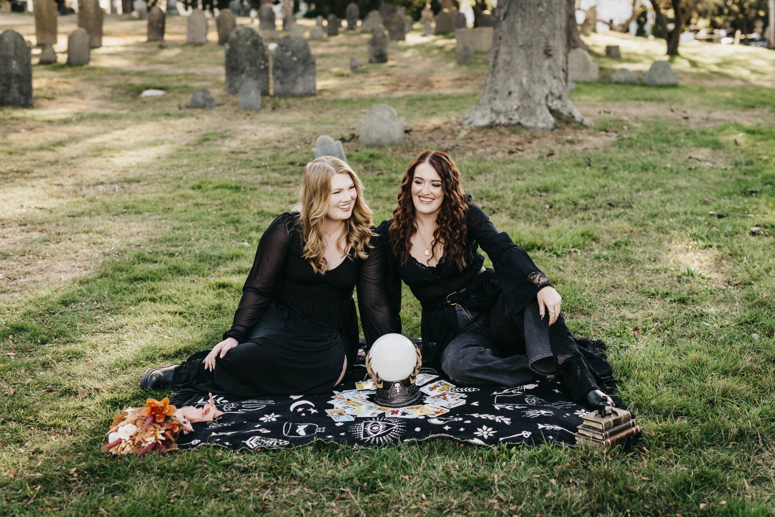 two girls in black sitting on a picnic blanket in a cemetery in salem massachusetts